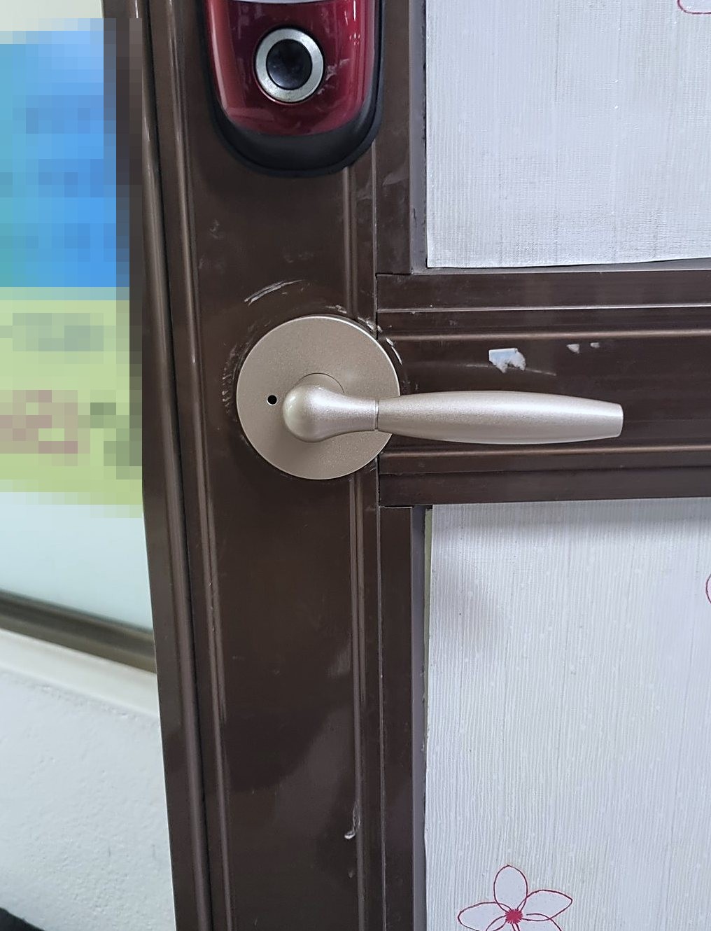 영종구 영종동 출장 — 갈색 알루미늄 틀 문에 붙은 붉은 몸체 도어락과 그 아래 연한 금빛 레버 손잡이